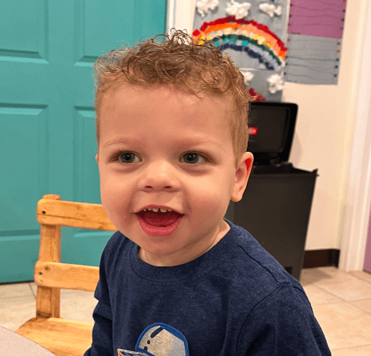 Smiling boy sitting at a table in a Christian childcare classroom in Las Vegas with art on the walls behind him.